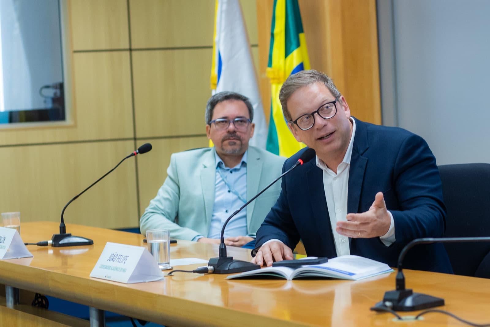 Coordenador acadêmico do MBA comentando o livro na mesa, ao lado de outro participante