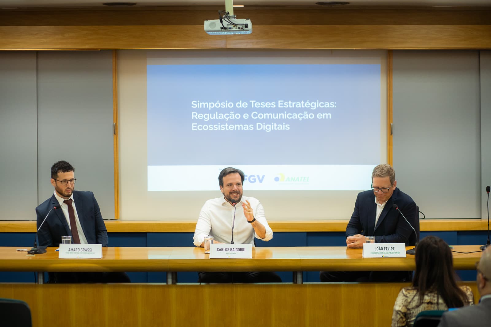 Mesa do Simpósio de Teses Estratégicas da FGV e da ANATEL, em Brasília, com o telão do evento ao fundo