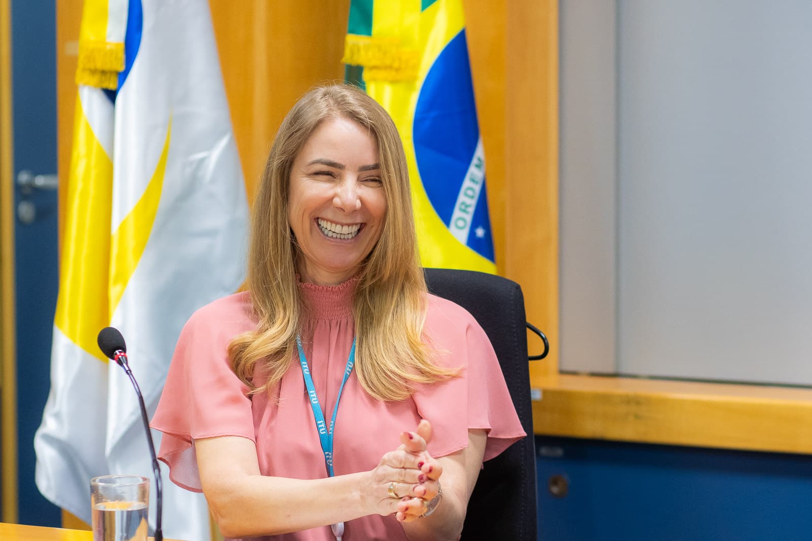 Participante sorrindo na mesa, com as bandeiras ao fundo